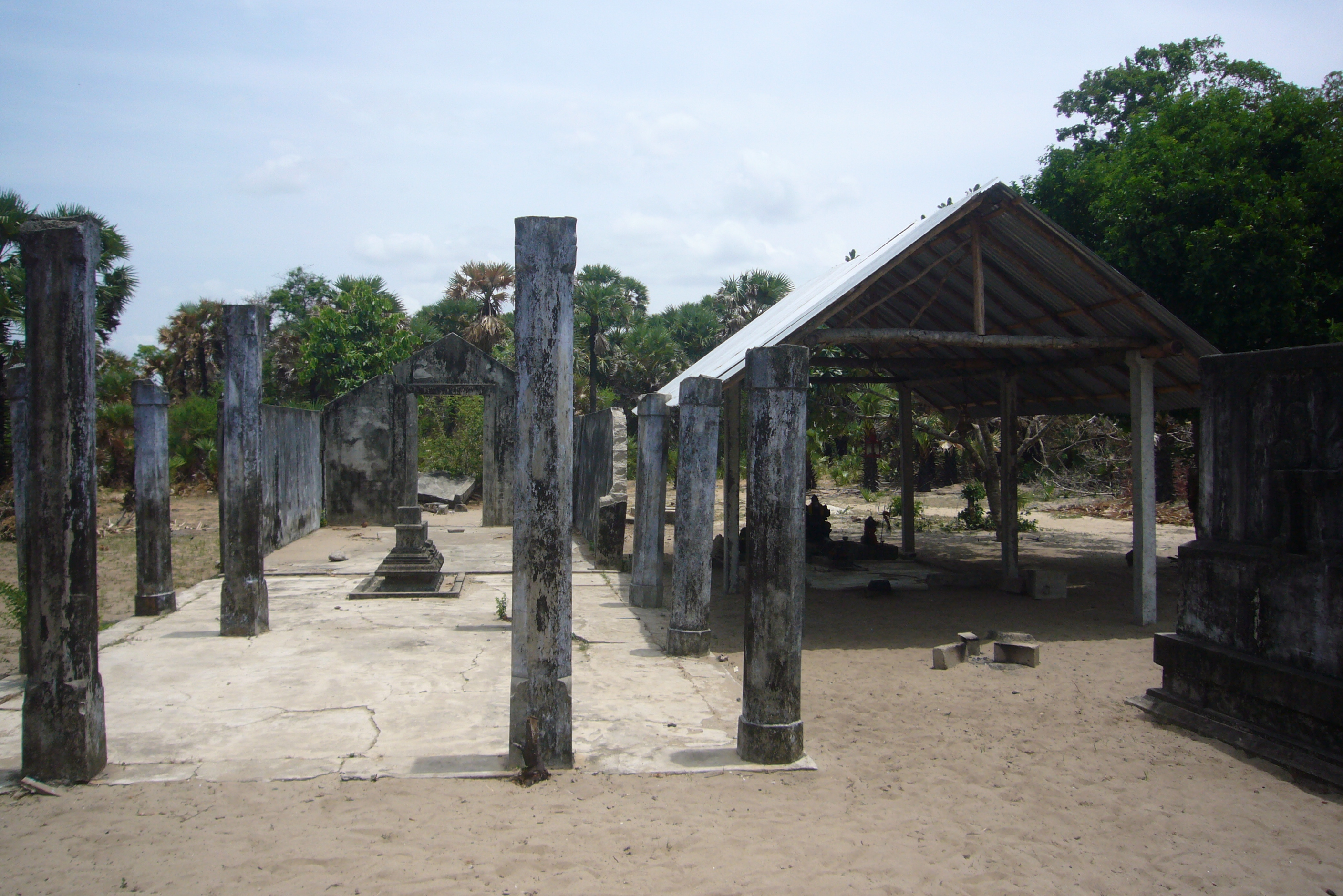 柱だけ残る旧寺院に隣接して立てられたトタン屋根葺きの新寺院